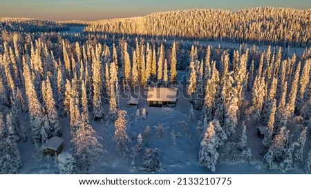 Aerial drone view of a cabin in snowy, winter forest, sunny morning sunrise, in Lapland