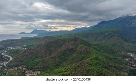 Aerial drone view of the city at the foot of the green mountains. It's a nasty day. Sunbeams between the clouds. High quality photo - Shutterstock ID 2240130439