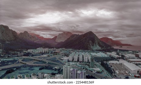 Aerial drone view of the city at the foot of the green mountains. Clear sunny day. White clouds. Green hills. - Shutterstock ID 2254481369
