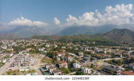 Aerial drone view of the city at the foot of the green mountains. Clear sunny day. White clouds. Green hills. - Shutterstock ID 2254481389