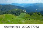 Aerial Drone view from Ciucas Peak and the pastures and forests surrounding it. Below there is a valley with human settlements. Capatanii Massif, Carpathians, Romania 