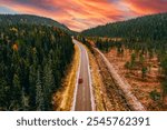 Aerial drone view of curved road with red car and fall forest with colorful leaves and spectacular sky in Finland, Lapland.