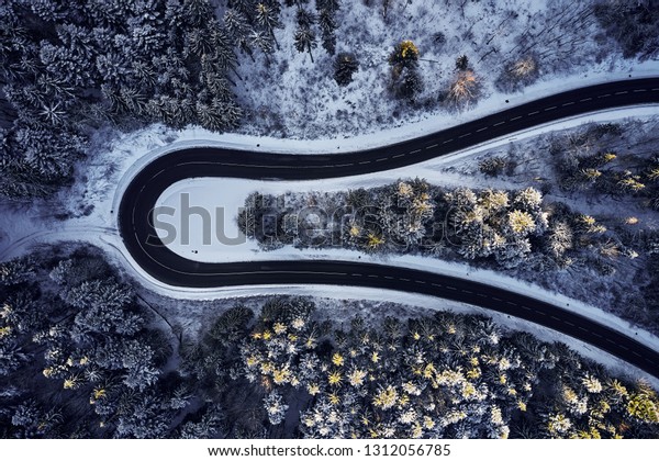 Aerial drone view of a curved winding\
road through the forest high up in the mountains in the winter with\
snow covered trees and curved streets in\
winter