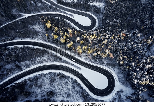 Aerial drone view of a curved winding\
road through the forest high up in the mountains in the winter with\
snow covered trees and curved streets in\
winter