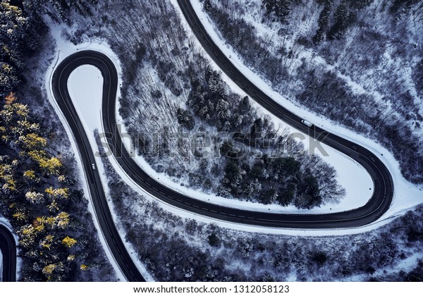 Aerial drone view of a curved winding
road through the forest high up in the mountains in the winter with
snow covered trees and curved streets in
winter