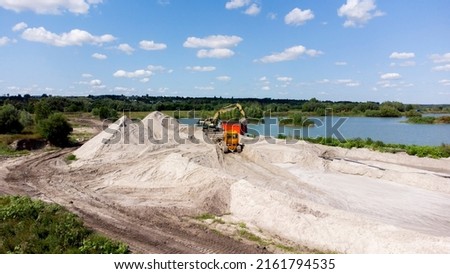Aerial drone view flight over sand mining. Sand quarry. Top view. Lake with blue water near sand pit. Bulldozer machine moving sand in quarry. Mining industry. Mining equipment at quarry.