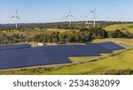 Aerial drone view of a hybrid solar and wind farm showing the large wind turbines in the background for renewable clean energy supply located at Bannister, NSW, Australia on a sunny day