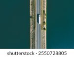 Aerial drone view of large freight transporter semi-truck driving on the bridge road over blue sea lake river