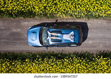 Aerial Drone View Of Man Relaxing On Car Roof. Male Enjoying Sun And Taking A Break During Travel