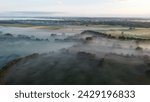 Aerial drone view of meadow landscape in The Netherlands on a sunny, foggy morning during blue hour. Misty low clouds, farmland landscape captured from above.