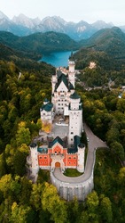 Aerial Drone View Neuschwanstein Castle On Alps Background In Vicinity Of Munich, Bavaria, Germany, Europe. Autumn Landscape With Castle And Lake In Mountains Covered With Spruce Forest