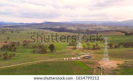 Aerial drone view of newly constructed electric transmission towers and overhead powerlines on mountainous green fields at Strathnairn in Canberra, the capital city of Australia, in the late afternoon