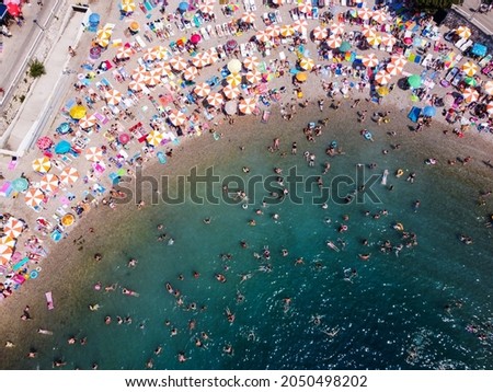 Aerial drone view of overcrowded sea and beach during peak of tourist season. Crowd of people swimming in the sea at summer. People in swimsuit bathing. 