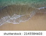 Aerial drone view taken directly above of a pure white sand beach facing waves breaking along the shoreline of a lagoon. That image was taken in Bali Indonesia.