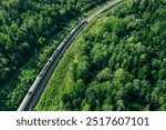 Aerial drone view of train in beautiful green summer forest. Long commuter train moving to railway station