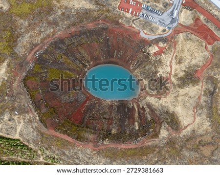 Aerial drone view of Kerið volcanic crater in Iceland. The striking red volcanic slopes surround a vivid blue crater lake, creating a dramatic contrast in the Icelandic landscape. Famous natural landmark on the Golden Circle, ideal for travel, geology, and nature-themed content.