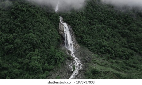 Aerial drone view of waterfall between trees on high hills during misty morning. Water flows down to rocky mountain. Breathtaking scenic landscape background. Moody green woods and grey stones