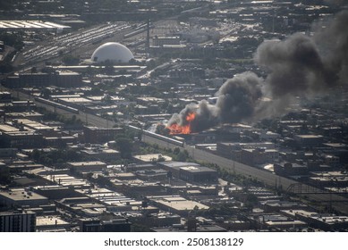 aerial elevated view of a massive building on fire, engulfed in flames in a dense urban environment with smoke billowing into the air