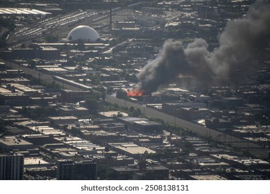 aerial elevated view of a massive building on fire, engulfed in flames in a dense urban environment with smoke billowing into the air