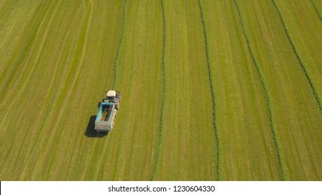 AERIAL: Farmer In Tractor On Farmland Field Collecting Fodder In Forage Wagon