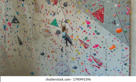 AERIAL: Fit Young Teenager Lead Climbs Up A Challenging Route In Otherwise Empty Indoor Rock-climbing Training Center. Athletic Caucasian Girl Prepares For A Climbing Competition By Training Indoors.