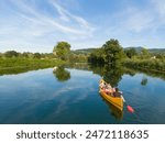 AERIAL: Flying behind a group of tourists canoeing along a calm river running past an old church. Young friends spend a sunny summer day by going on a canoeing trip down the tranquil river Krka.