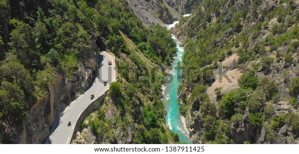 AERIAL: Flying high above cars and motorcycles\
entering a dark tunnel above a deep gorge in France. Tourists on a\
scenic road trip on motorbikes and in cars drive above a river in\
sunny French Alps.