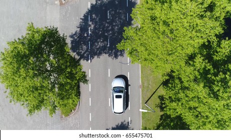 Aerial following car top-down view this grey colored station wagon is driving over two way street with green trees on both sides of street
