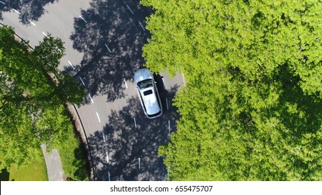 Aerial following car top-down view this grey colored station wagon is driving over two way street corner green trees on both sides of street
