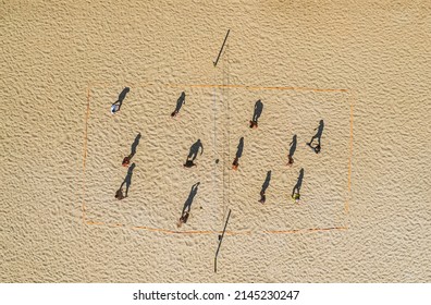aerial footage from a drone of people playing beach volleyball on the shore. Flat view from a height of the elongated shadows of people