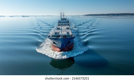 Aerial forward view of general cargo vessel making way ahead in Finnish archipelago during spring time. Glassy sea surface.