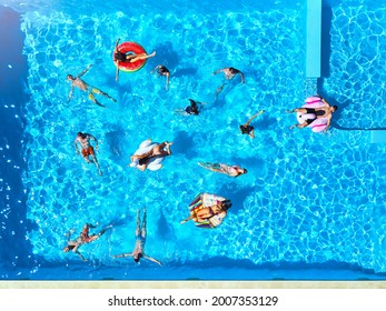 Aerial Of Friends Having Party In Swimming Pool With Inflatable Flamingo, Swan, Mattress. Happy Young People Relax At Luxury Resort On Sunny Day. View From Above. Girls In Bikini Sunbathing In A Sun.