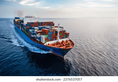 Aerial front view of a large container cargo ship traveling with speed over calm ocean and sunset light - Powered by Shutterstock