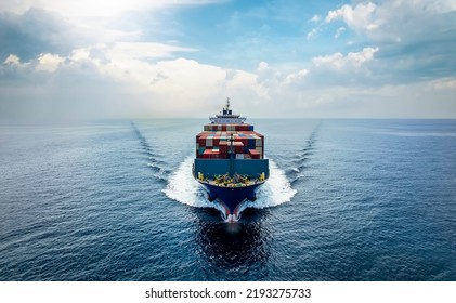 Aerial front view of a medium sized, loaded container cargo vessel traveling with speed over the ocean under cloudy sky