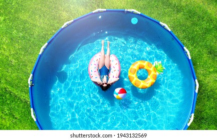 Aerial. Girl Resting In A Metal Frame Pool With Inflatable Toys. Summer Leisure And Fun Concept. Frame Pool Stand On A Green Grass Lawn. Top View From Drone.