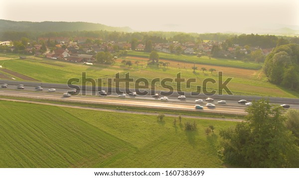 AERIAL: Golden afternoon sky illuminates the\
tranquil countryside for vehicles driving along the busy road.\
Picturesque drone view of cars and truck driving across the meadows\
on a beautiful morning
