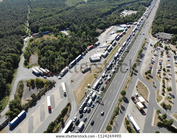 Aerial helicopter view from above of a highway with\
one direction fully filled with standing cars and trucks because of\
a traffic jam