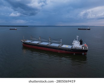 Aerial high-angle view of a large bulk carrier ship with cargo cranes sailing on the Baltic Sea with other vessels in the background at twilight.