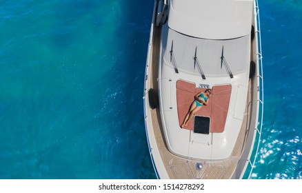 Aerial image of a blonde girl laying on the bow of the yacht and taking a photo of herself from the drone