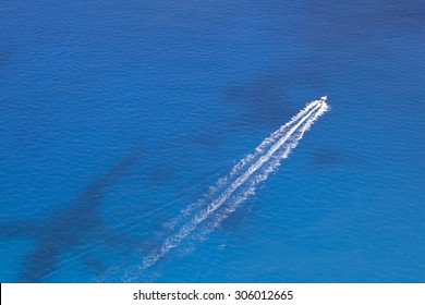 Aerial image of motorboat floating in a turquoise blue sea water. The boat is moving diagonally through the frame of the photo. 