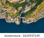 Aerial image of a narrow bridge over a small inlet on the Amalfi Coast, with cliffs, terraced greenery, buildings, and a secluded beach by the Tyrrhenian Sea.