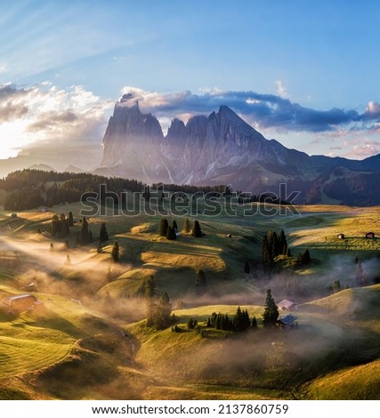 Aerial image of the Seiser Alm mountain in the Italian Dolomites after sunrise with golden light and fog