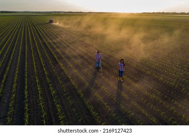 Aerial Image Of Senior Farmer Working With Hoe In Corn Field And Business Woman Supervising With Tractor In Background, Shoot From Drone