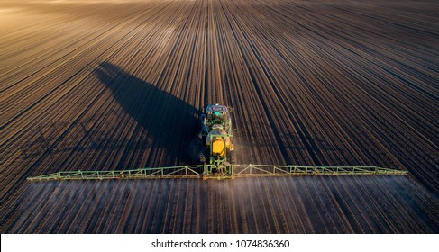 Aerial Image Of Tractor Spraying Soil And Young Crop In Springtime In Field