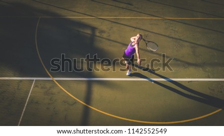 Aerial image of a young woman playing tennis on a tennis court shot from overhead with a drone