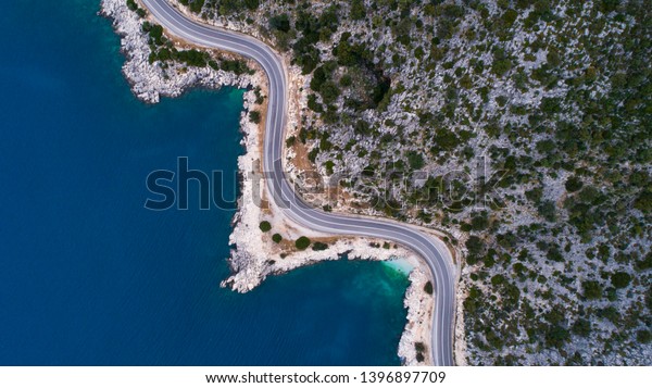 Aerial landscape of coastline and a road seascape. Car\
drives down the empty asphalt road running along the sunny\
Mediterranean shoreline of Turkey. Tourist car cruises down the\
scenic coastal road .