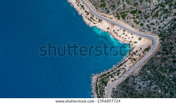 Aerial landscape of coastline and a road seascape. Car\
drives down the empty asphalt road running along the sunny\
Mediterranean shoreline of Turkey. Tourist car cruises down the\
scenic coastal road .