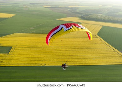 Aerial landscape: Colorful Paramotor seen from the sky over the fields of yellow rapeseed colza in spring. Essonne departement, Ile-de-France region, France