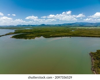 Aerial Landscape Of Seawater Flowing Into A Tidal Creek Surrounded By Tropical Vegetation Under A Cloudy Blue Sky With Mountain Range Background, St Helens Beach Queensland Australia