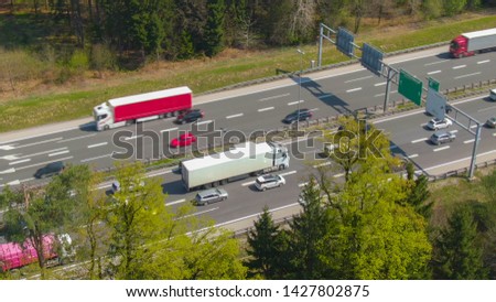AERIAL: Large white cargo truck carrying a shipping container gets stuck in traffic on the busy freeway. Countless cars surround the big lorry transporting a heavy freight container to its destination